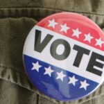 Big VOTE pin on top of clothing with white stars on red and blue background