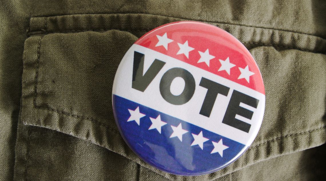 Big VOTE pin on top of clothing with white stars on red and blue background